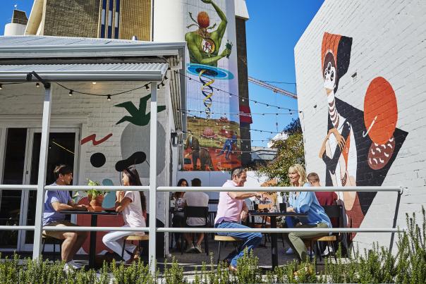 Groups of people eating, surrounded by street art on buildings