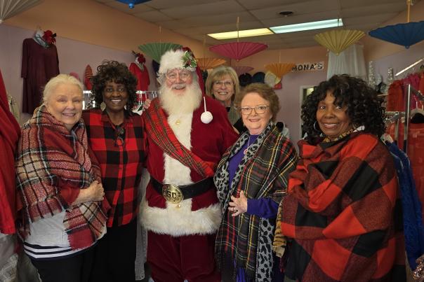 Five ladies wearing plaid tops pose with Santa.
