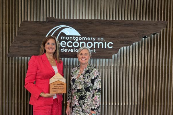 Two ladies in front of an economic development sign with one holding a plaque.