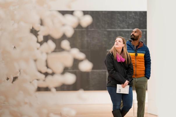 A couple walking through a museum exhibition staring wondrously upwards toward the show pieces