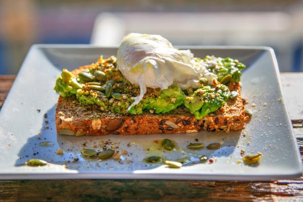 a white ceramic plate with a piece of seeded toast covered in smashed avocado and a poached egg