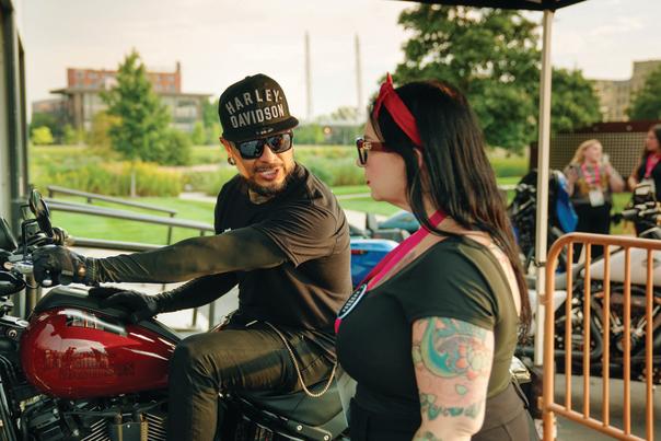 A motorcyclist on a red Harley-Davidson talks with an attendee outside during an event at the Harley-Davidson Museum.