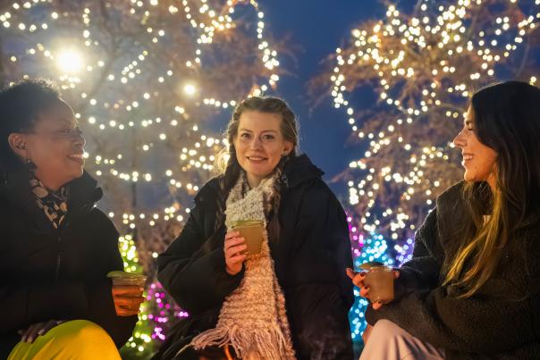 Three women sitting around a fire with lit trees in the background
