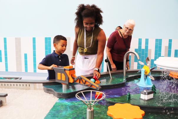 A young boy plays with the water feature while his mom and grandmother look on at the newly opened Sloan Museum of Discovery.
