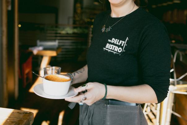 A smiling server holding a cup of soup at the Delft Bistro in Marquette, MI
