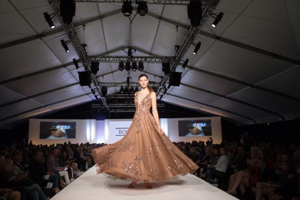 A model walks down the runway in a floor-length gown at Fashion Week El Paseo