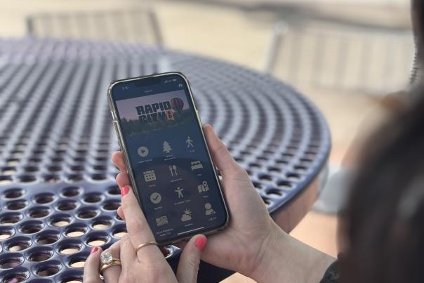 A woman holding her cell phone looks at the Visit Rapid City app while sitting at a picnic table