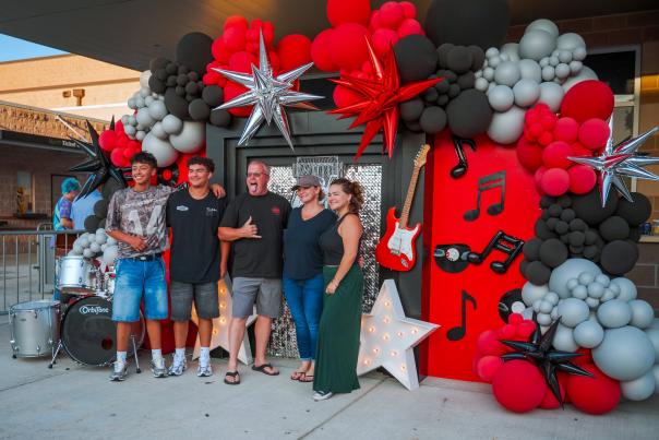 A family of five poses in front of a pop-up display for Led Zeppelin, featuring a bright red and black wall with a matching guitar, drum set, balloons, and inflatable music notes.