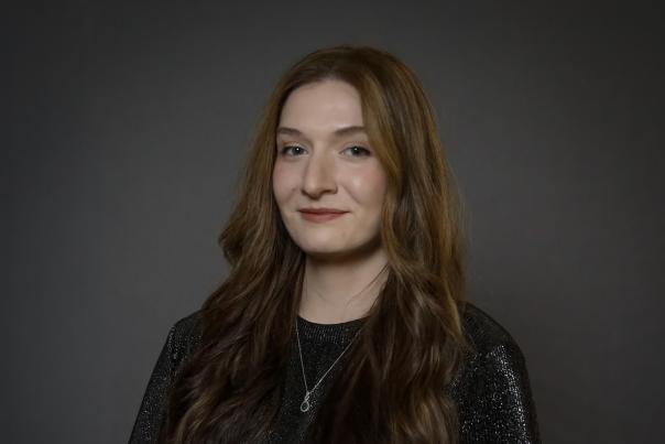 Caucasian lady in a black top poses for a headshot in front of a dark gray backdrop