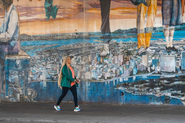 Shayla Bang walking by an Oakland, CA mural