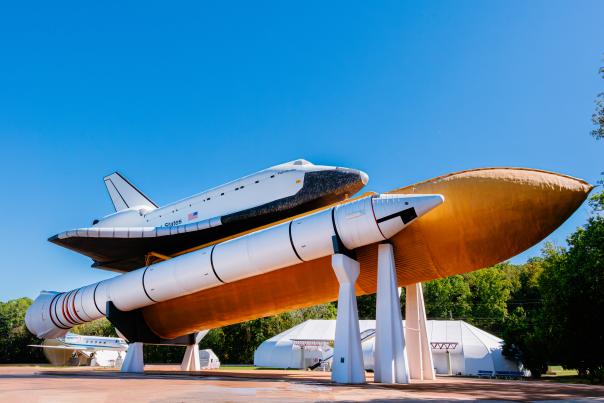 The Space Shuttle Pathfinder is displayed atop a full-scale external tank and solid rocket boosters at the U.S. Space & Rocket Center in Huntsville. The shuttle and rocket stack stand against a clear blue sky, showcasing the scale and engineering of NASA’s Space Shuttle program.