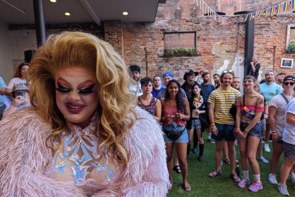 A drag queen in pink feathers and a shiny top with a crowd behind her