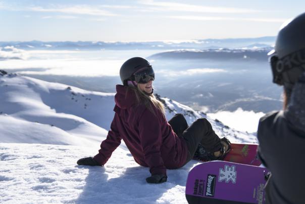 Lady snowboarder resting at the top of the mountain
