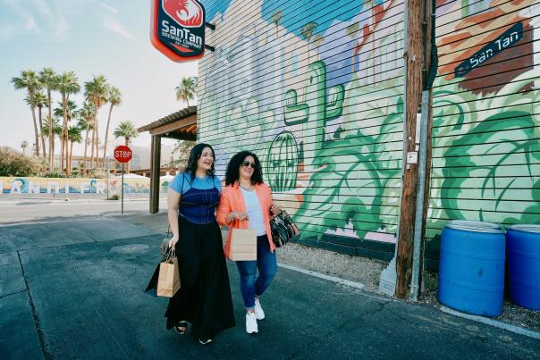 Mother & daughter walking past SanTan Brewing mural with shopping bags.