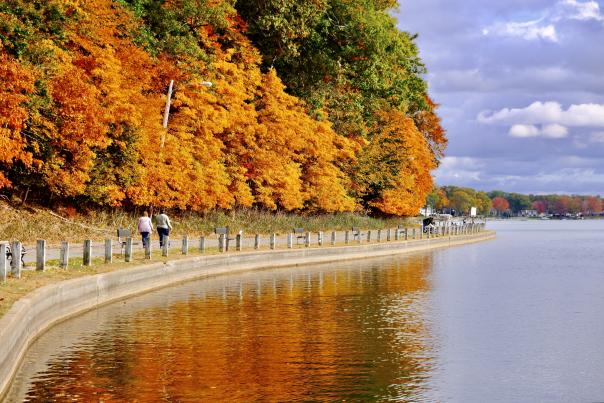 two people walking along lakeside trail with fall foliage reflected in the water