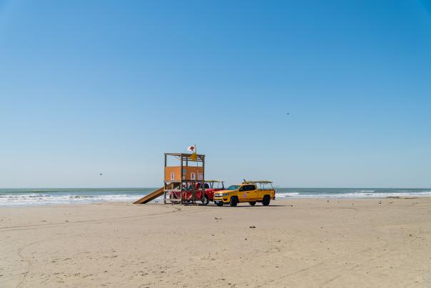 A yellow lifeguard tower and a truck on a sandy beach in Port Aransas under a clear sky.