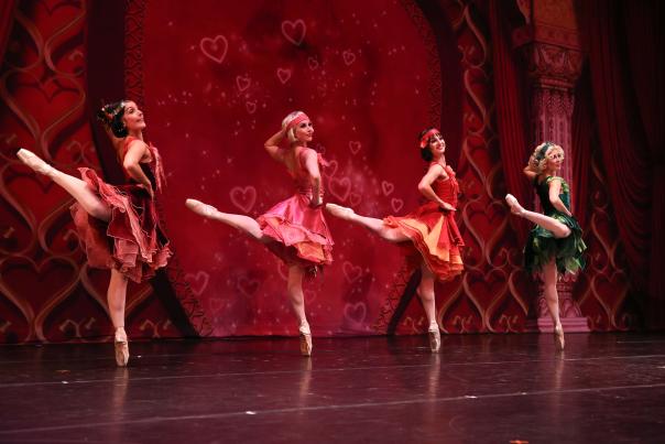 Four dancers in front of a red heart backdrop.