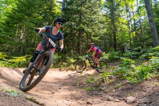two mountain bikers ride around a forested trail curve