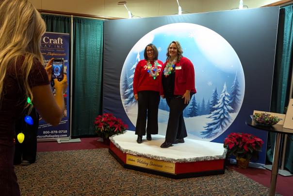 Two women in front of a snow globe backdrop dressed in holiday clothes.