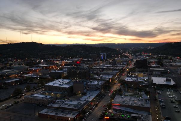 Aerial view of a city during a sunset, with vibrant orange and pink hues in the sky. City lights are just turning on, creating a lively, urban atmosphere.
