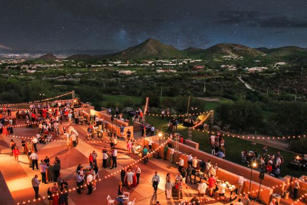 aerial view of a large meeting on the patio of JW Marriott Starr Pass Resort. Mountain-view landscape with star-filled sky lights the background