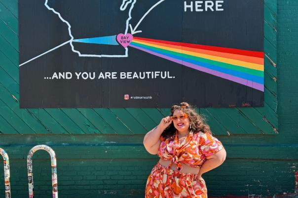 Alysse Dalessandro poses beneath a Bay View mural mapping the Milwaukee neighborhood with a rainbow and the words, “You are here … and you are beautiful.”