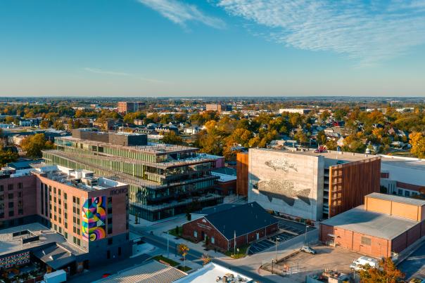 Aerial view of a vibrant urban landscape featuring modern buildings, colorful murals, and tree-lined streets under a clear blue sky.