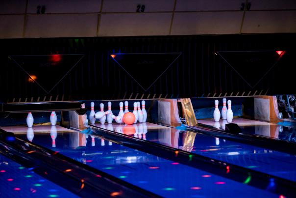 Orange bowling ball hitting pins on a bowling alley lane