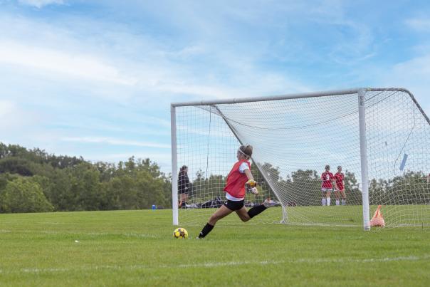 A female goalie kicking a soccer ball away from the goal.