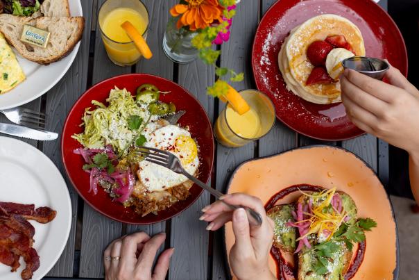An overhead view of a table full of bright colored plates with various breakfast dishes and glasses of orange juice being served.