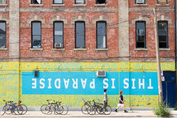 People walk by a wall mural that reads "This is Paradise" in Toronto's Queen Street West neighbourhood