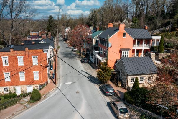 Aerial view of a Waterford, Virginia lined with historic brick and colorful houses, surrounded by trees and parked cars under a blue sky.