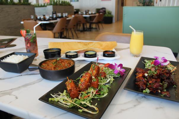 A table full of food from Aahaa Indian Cuisine, including: chicken vindaloo, paneer lollipops, dragon chicken, masala dosa, a berry mojito and a mango lassi