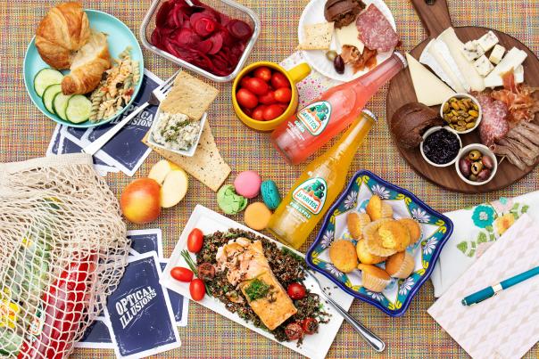 bottled sodas, charcuterie board with meats and cheeses, and various other foods on a table with cards.
