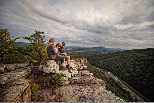 A mom, dad and son sit on a shale cliff overlooking a mountain vista.