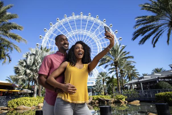 A couple posing for a selfie in front of The Wheel at ICON Park