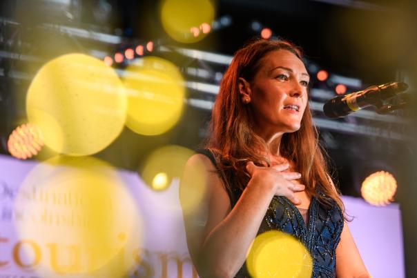 a woman stood at a podium in a dress speaking to a crowd of people - off camera