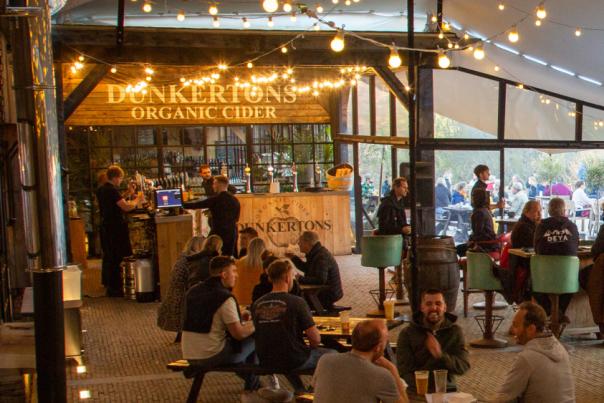 A group of people sitting around tables under a large marquee with fairy lights strung from the roof