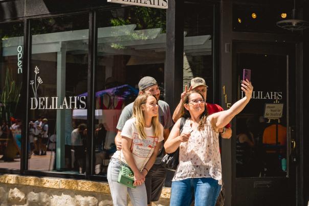 Smiling family taking a selfie in front of Delilah’s restaurant entrance