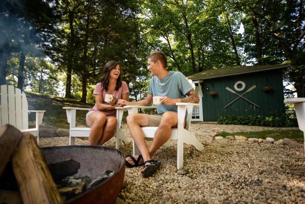 Couple laughing while drinking coffee by a campfire