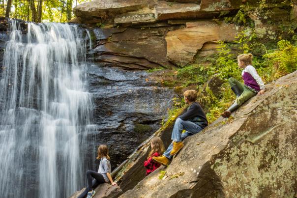 Four children sitting on a rock next to waterfall