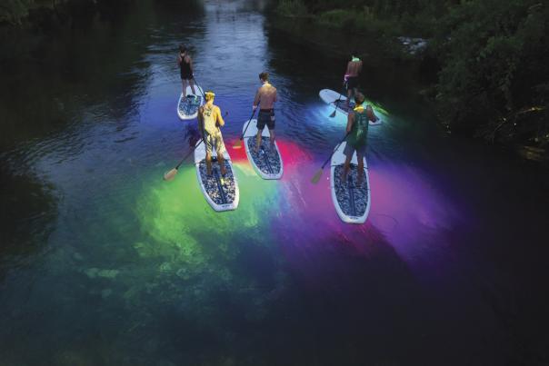 Group on glowing stand-up paddle boards at night