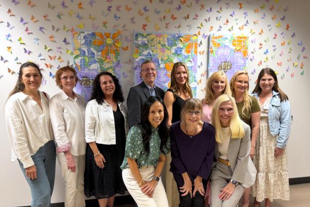 TWAC Board and Staff, with local artist Sandra Cooper, pose with the community mural that Cooper designed. The mural is displayed at Canopy Cancer Survivorship Center at Hermann Memorial - The Woodlands. It consists of tiles painted with brightly colored flowers, surrounded by paper butterflies with hopeful messages on their wings.