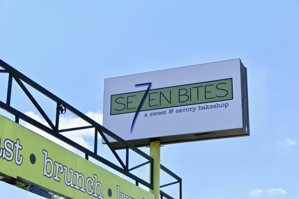 A large white and green sign with the Se7en Bites logo stands above a lime green arch, with blue skies behind it, in Orlando, Florida.