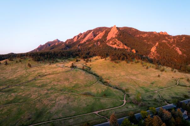 An aerial of the Flatirons at sunrise with trails and red tint to the mountains