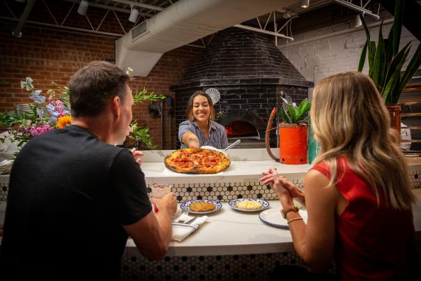 A server placing pizza in front of two customers at The Hall's Pizza Kitchen