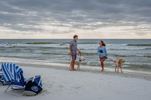 couple walking their two leashed dogs on the beach