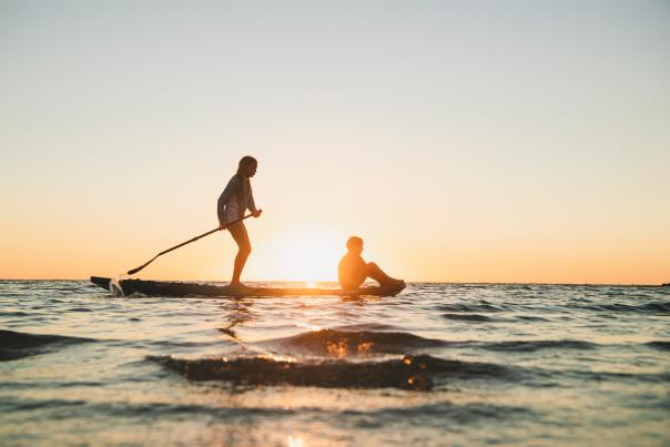 two girls on a paddleboard right as the sun is going down.