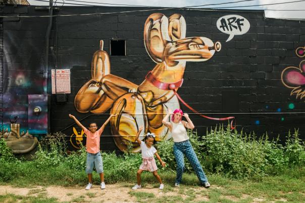 Woman and two kids pose in front of a mural in Downtown San Marcos, TX.