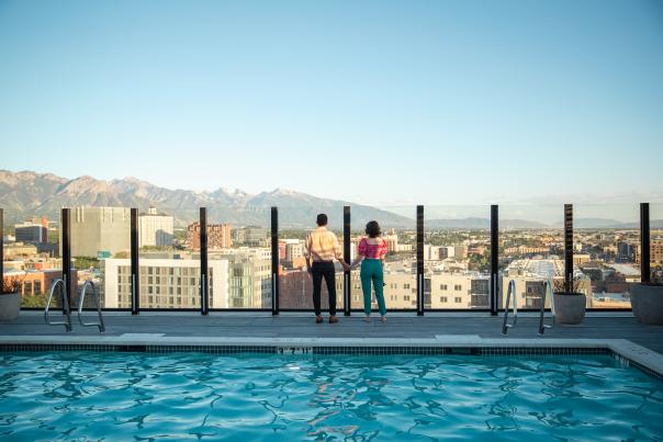 View of downtown Salt Lake looking across a pool with 2 people standing near the edge overlooking the city